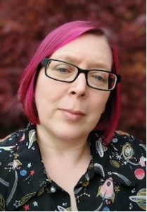 Head shot of Dr Char Goodwin who has pink hair and glasses and is wearing a space themed shirt