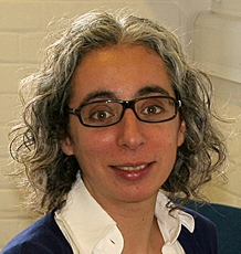 Head shot of Prof Manuela Barreto who has curly hair and is wearing glasses and a white shirt and blazer.