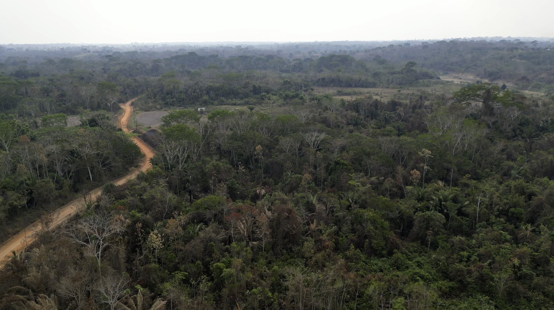 A dirt road cutting through fire-degraded Amazon forest, with cleared pasture beyond and smoke haze on the horizon, Acre, Brazil