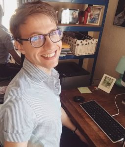 Picture shows Dr Richard Vytniorgu. He is at his desk, wears glasses and a short-sleeved button-up shirt and is smiling showing teeth.