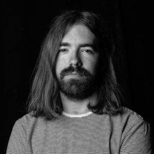 Picture shows a black and white portrait of Scott, who is pictured with shoulder length hair and a beard.