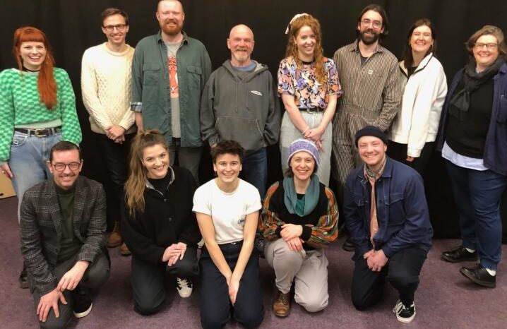 A posed group photo of some of the project and creative team. Eight people stand in a line, with five people posing crouched in front. Lots of smiles.