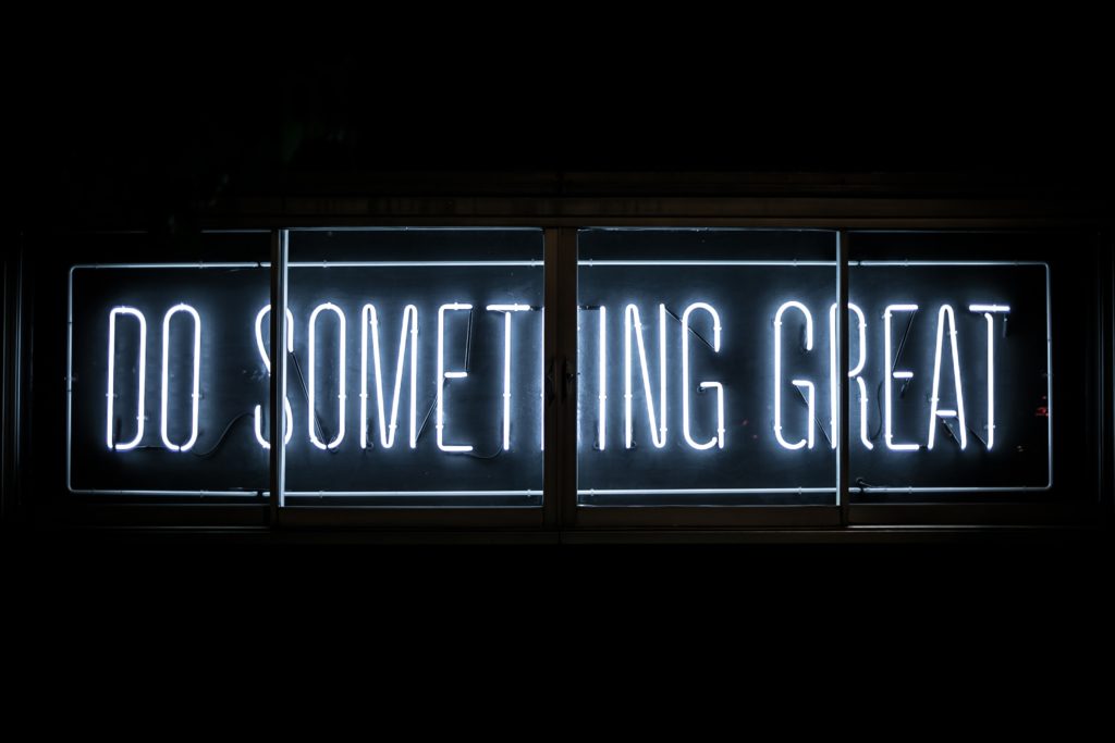 A white neon sign against a black background. The sign says do something great.