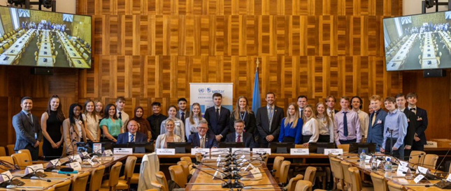 Officials from the UN, the University of Exeter, and university students are formally dressed in a wood paneled inside the UN.