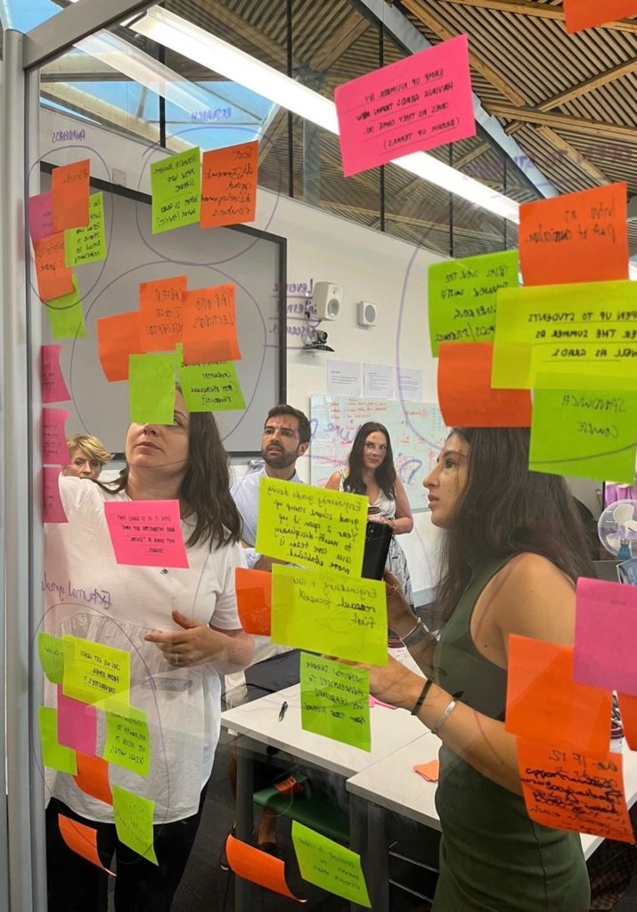 People behind a perspex board covered in multi-coloured sticky notes brainstorming ideas