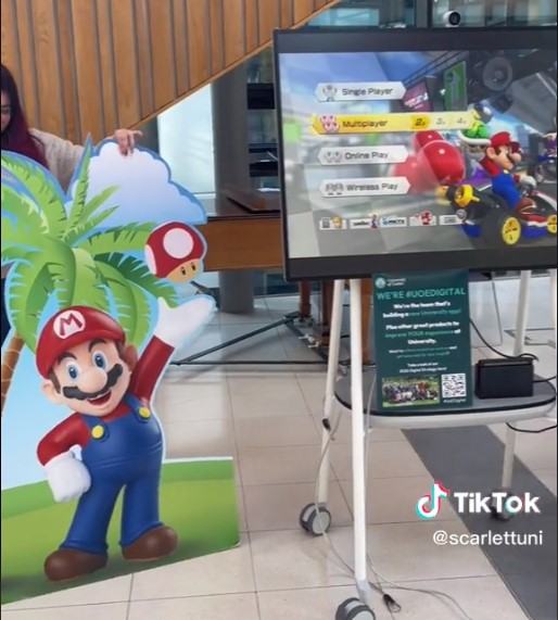 TV with the Mario Kart game start screen. There is a Mario Kart cardboard cut out next to the screen