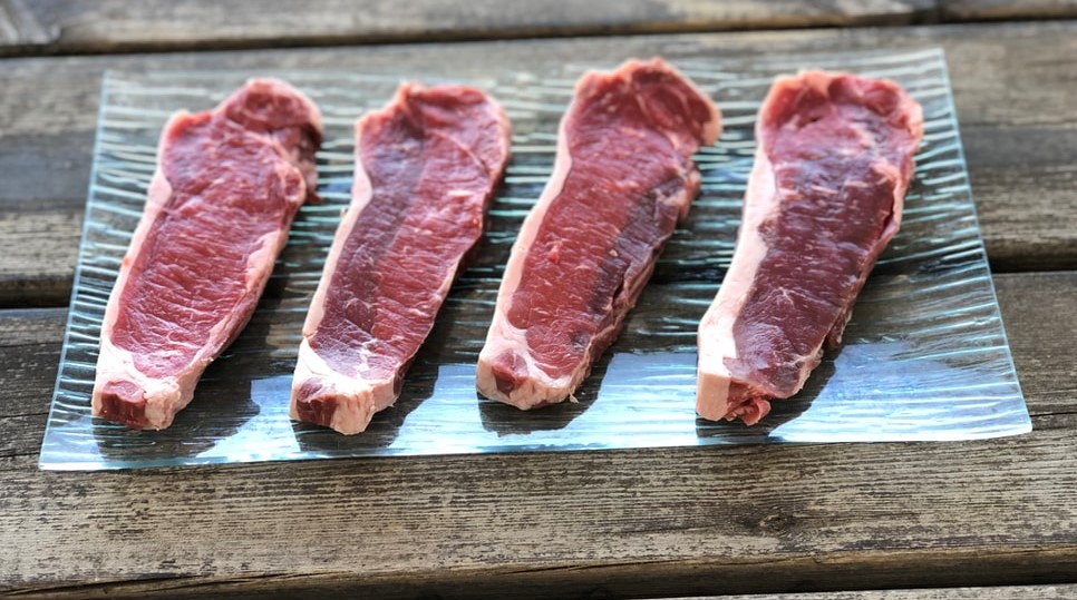 Four raw meat steaks on a wooden table