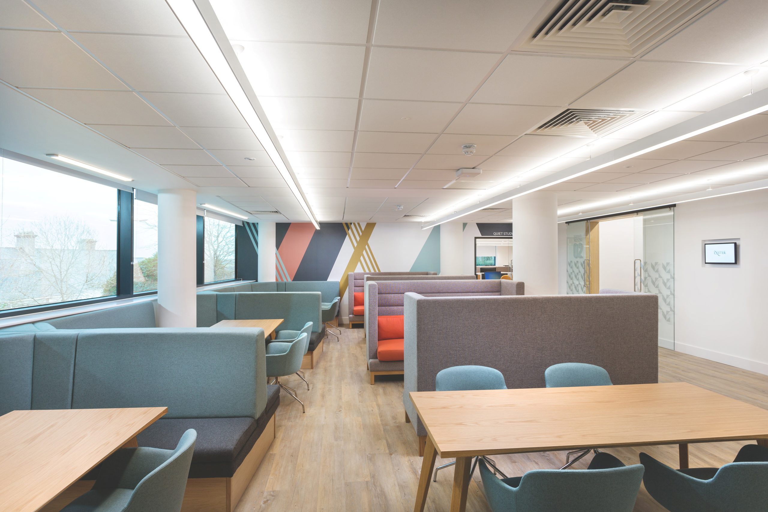 Group study areas in the masters suite. A bright, modern room filled with large wooden tables surrounded by chairs and sofas.