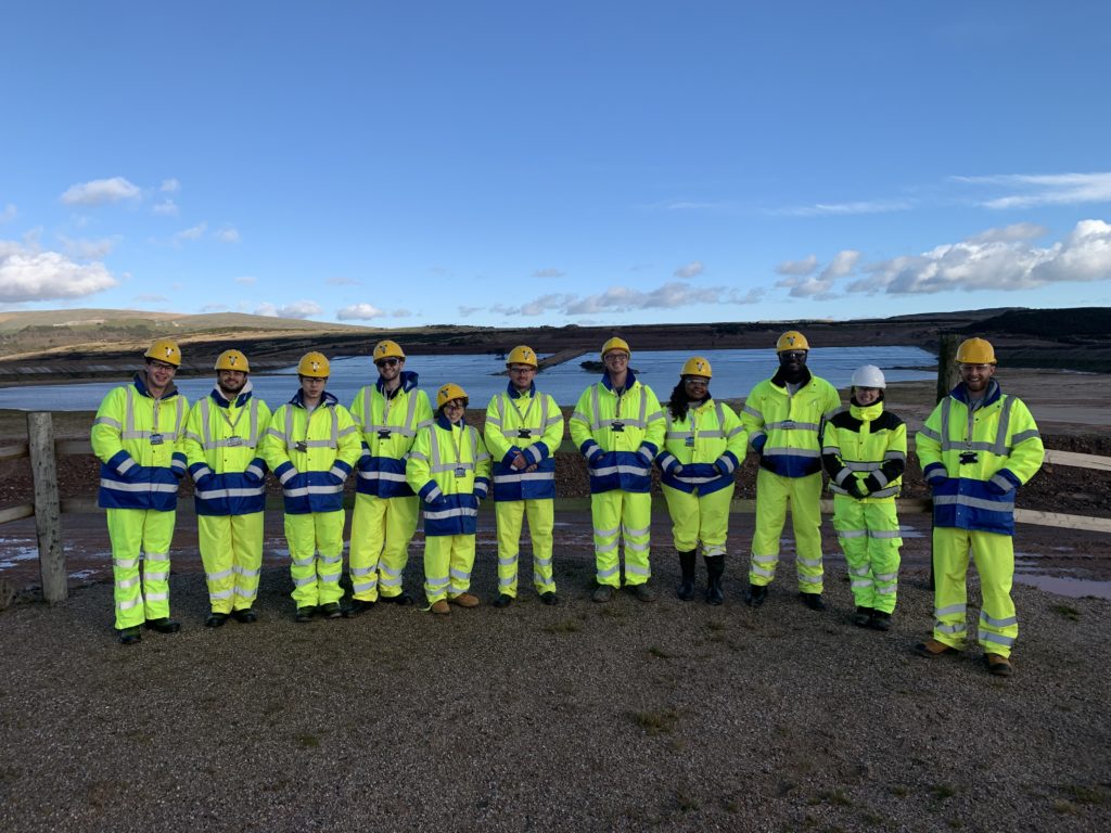 Eleven students dressed in high-vis PPW in front of a body of water during their visit to Tungsten West mine. 
