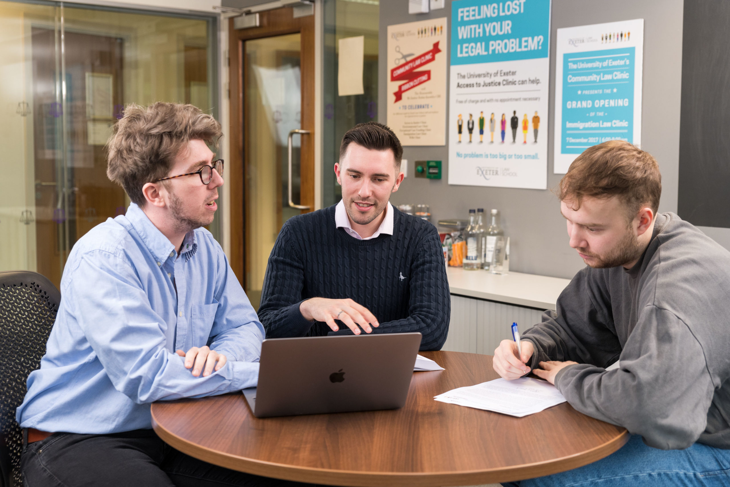 Students sit around a table with a laptop discussing together