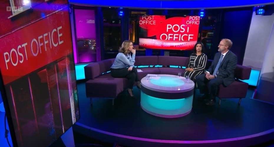 Picture of a television studio at BBC Newsnight. The backdrop shows images of the Post Office logo. There are three people sat on a purple sofa and there is a glass table in front of them