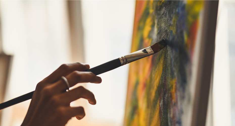a hand holding a paintbrush to a canvas with a mixture of colours