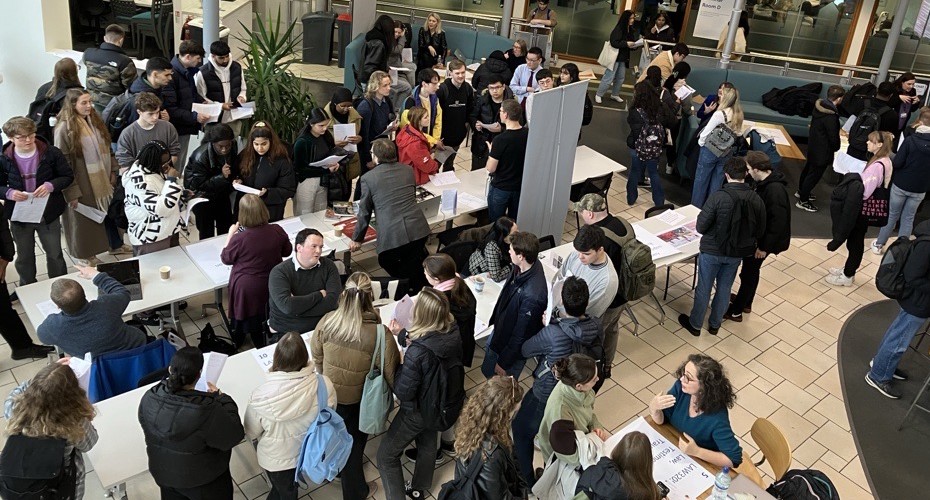 An aerial view of students attending a module fair which is laid out between tables with tutors at each one chatting to the attendees.