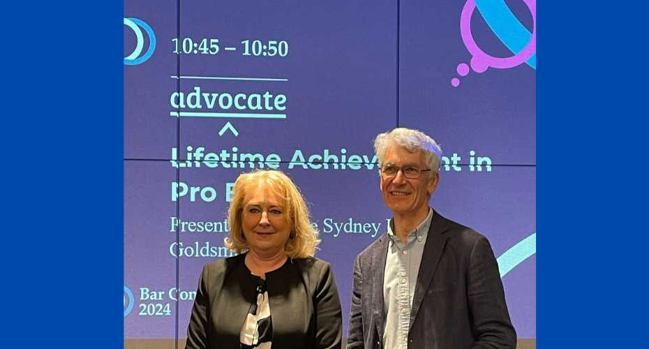 Two people stood in front of a project image at an awards ceremony. The wording in the background reads Lifetime Achievement in Pro Bono.