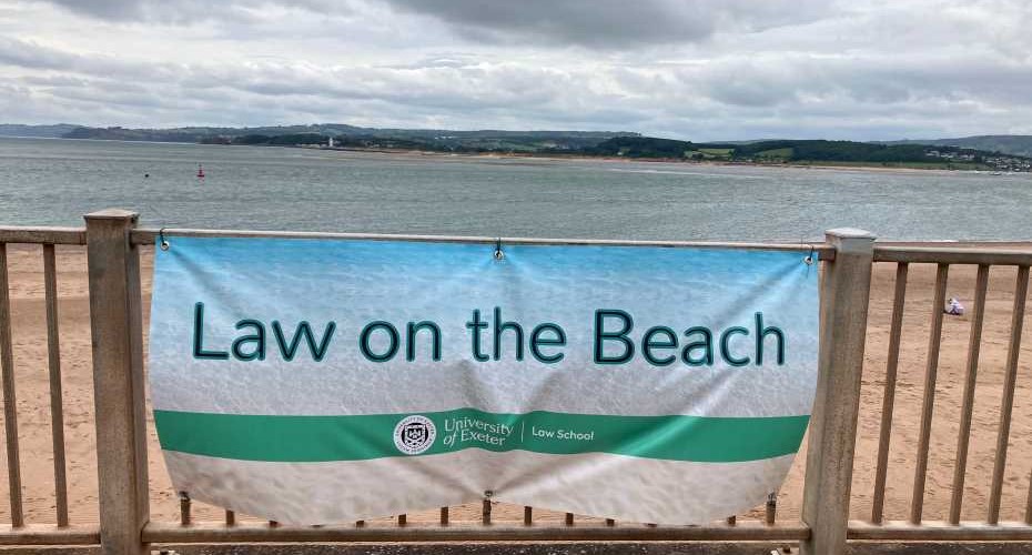 A banner on a fence which says law on the beach. in the background is the sea and a headland.