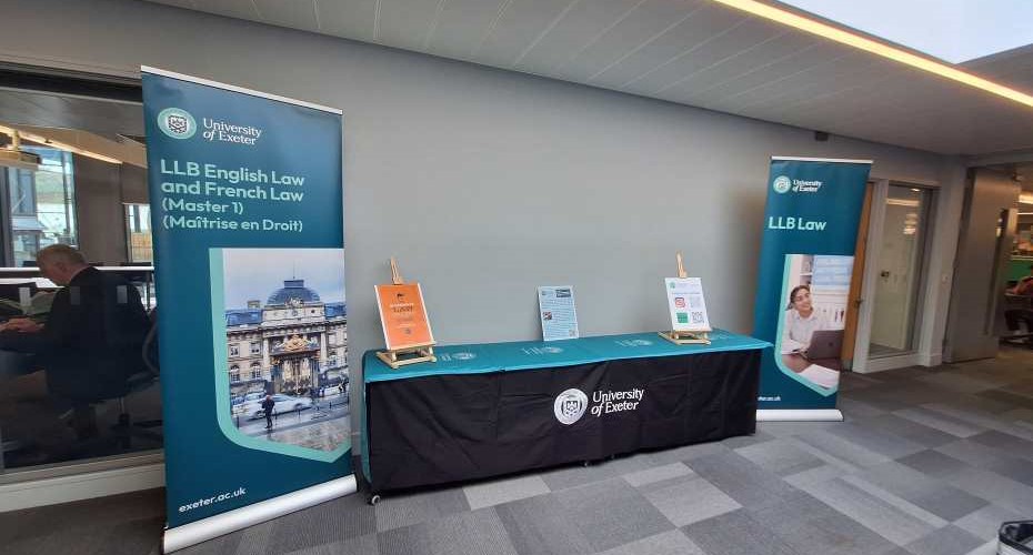 A long table with a green university of Exeter cloth, and 3 display A frames. There are two pull up banners promoting the exeter Law school