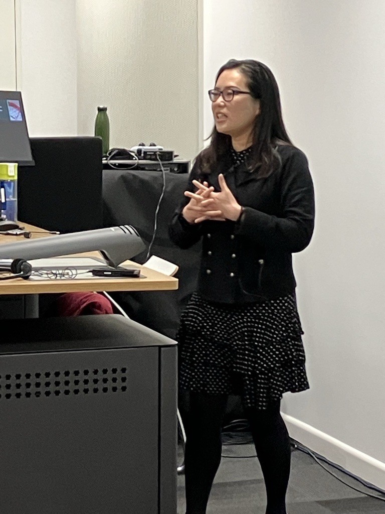 Dr I-Ju Chen standing in front of a desk presenting a lecture 