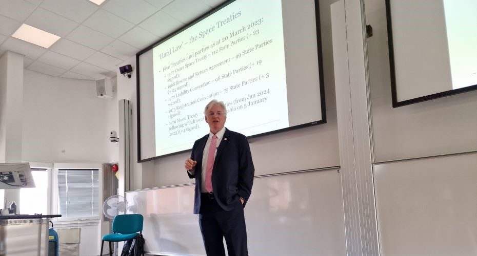 Professor Dale Stephens stood at the front of a lecture room with a slide backdrop which says Hard Law - the Space treaties