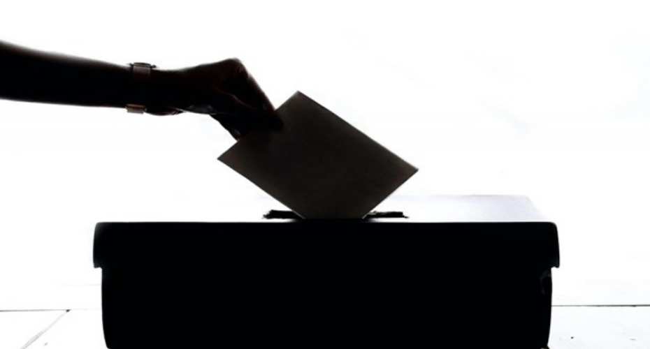 a silhouette of a hand holding a ballot paper dropping it into a box