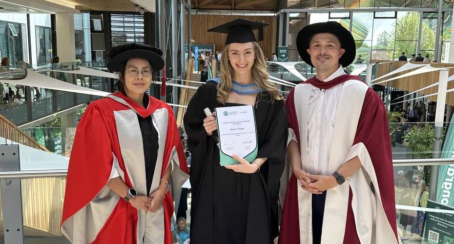Prize winner Bethan Morgan alongside Amy Man and davcid Yuratich. All are wearing graduation robes and Bethan is holding a certificate.