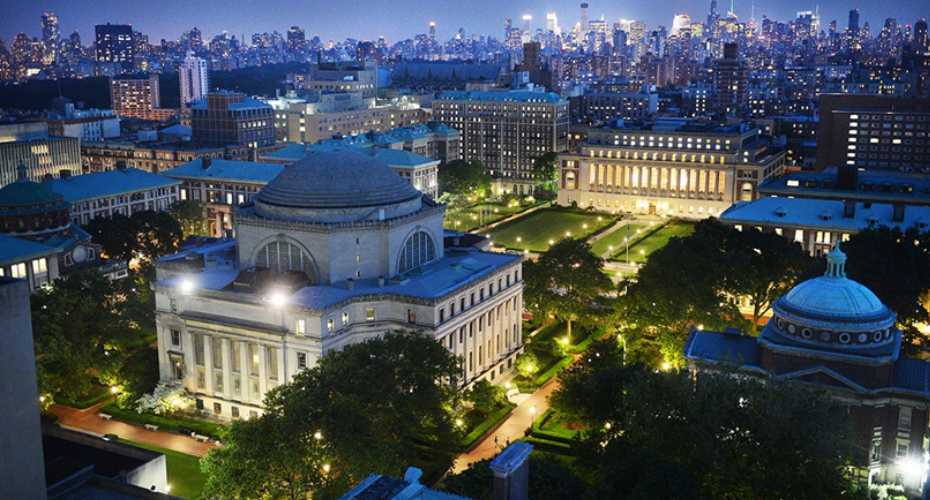 city view over Columbia Law School. You can see various historic buildings. The one in the centre of the picture has a domed top and is lit up from beneath. There are trees and gardens around it.