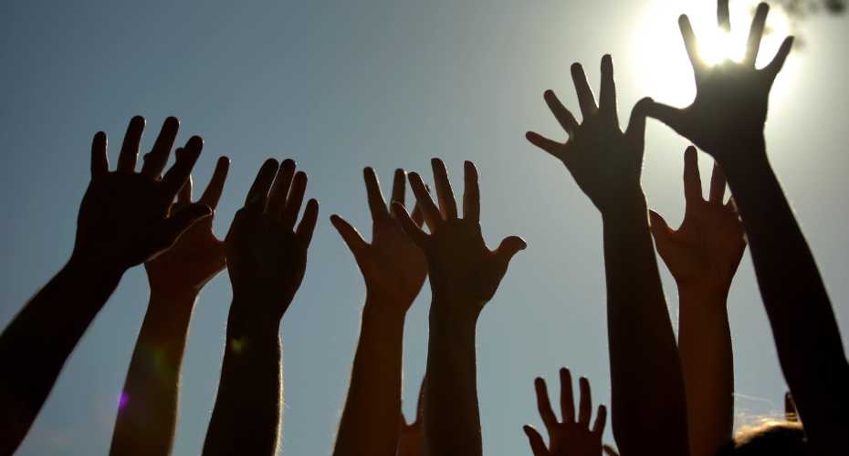 A row of upstretched hands, silhouetted against a sunny sky