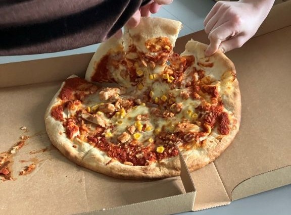 a pizza with tomato and chilcen pieces on. A hand is reaching to tear it into pieces