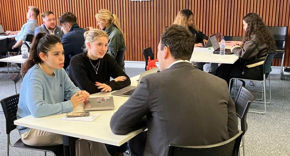 Two students sat chatting across a desk with a Clinic supervisor with laptops in front of them.