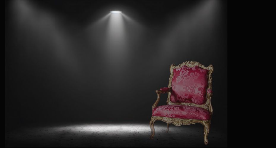 A dark room with a red fancy chair and a spotlight overhead