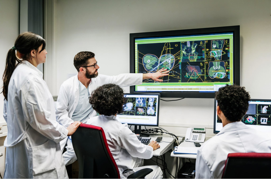 Image of two women and two men in white lab coats looking at a screen with anatomical images on it. One of the men is pointing at the screen as if teaching.