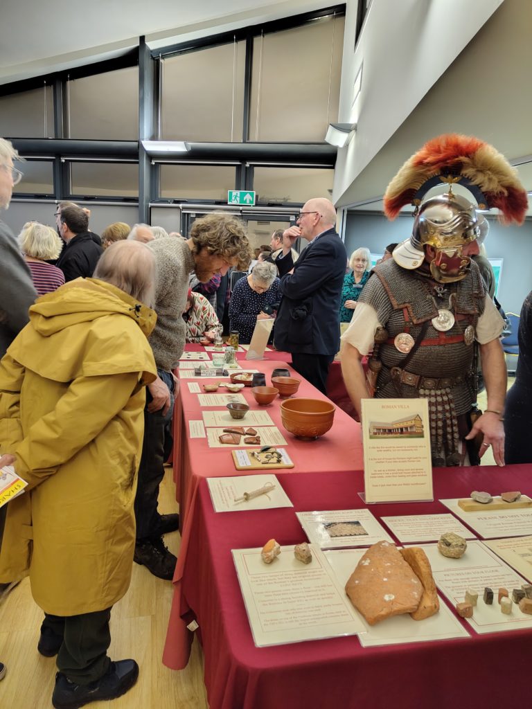 Visitors look at the displays about Roman life and villas, while a person dressed as a Roman soldier chats.