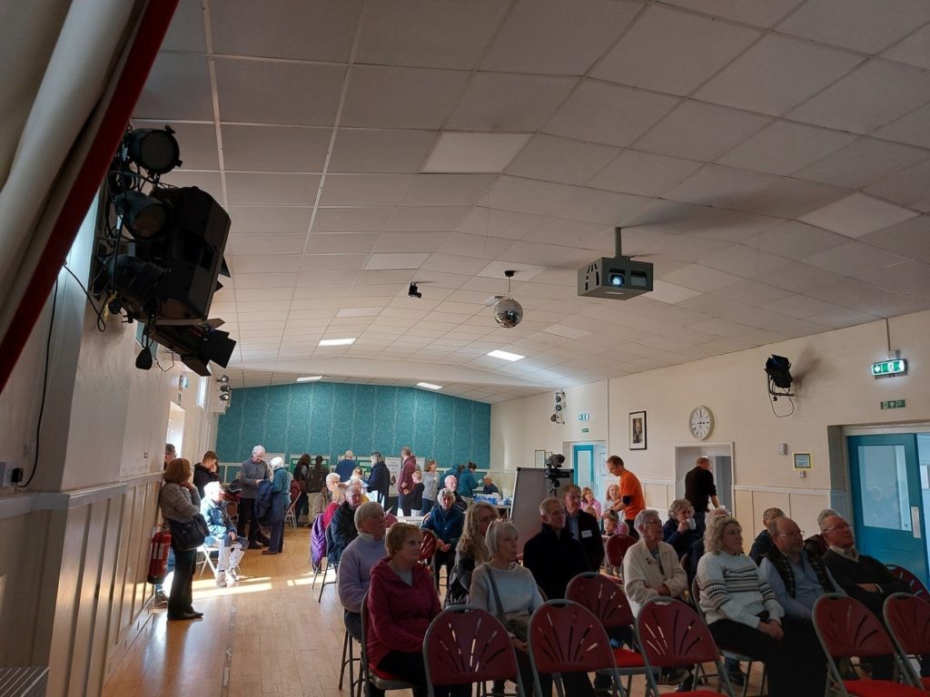 Inside the hall, people are seated and standing around the edge looking at displays