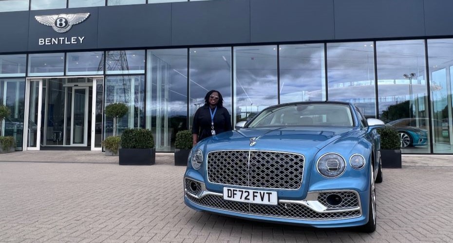 Student standing next to a blue car in front of the Bentley building