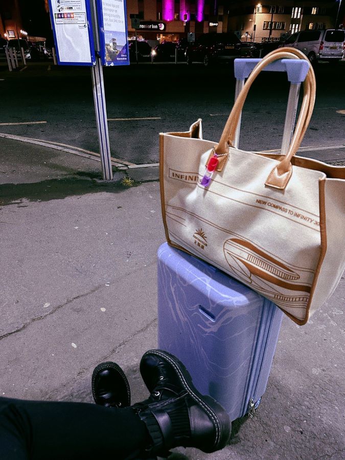 Photo taken when waiting for a bus at night with a blue suitcase, beige tote bag and wearing chunky black books