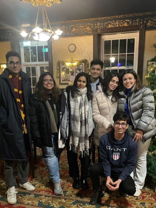 Group of students in winter coats in a room with a Christmas tree.