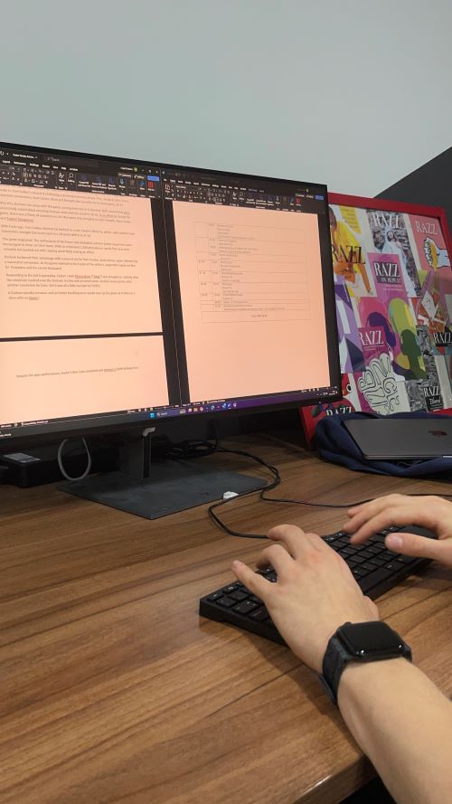 Two hands typing on a keyboard in front of a desktop open on two Word documents on top of a wooden workbench