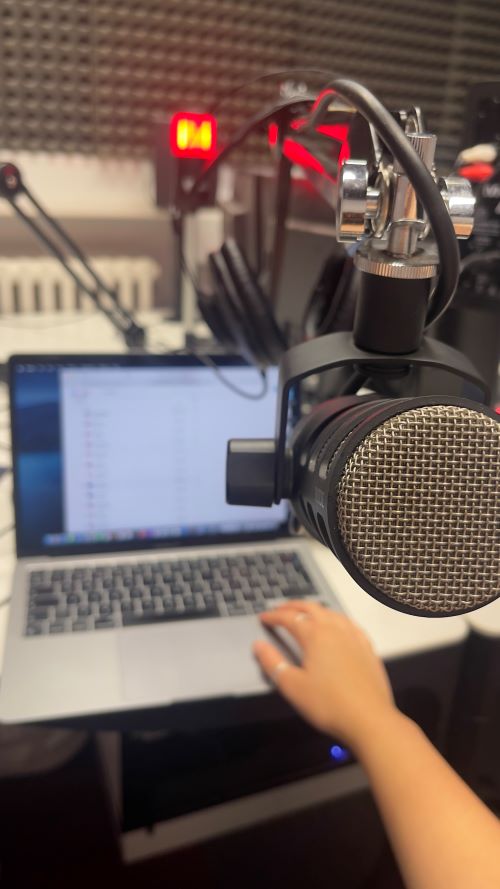 'Point of view' photo of a radio microphone in front of a laptop and a red recording light