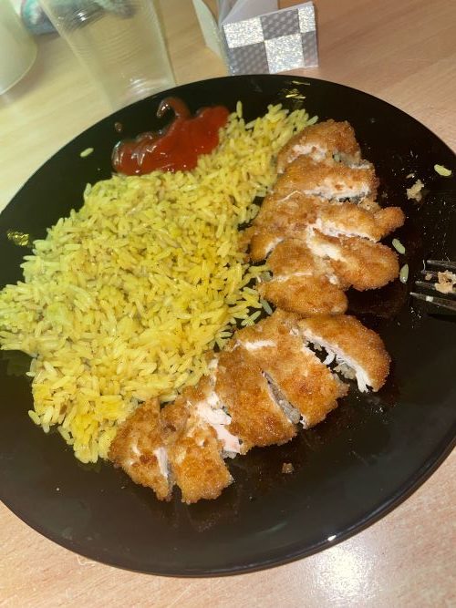 Breaded chicken cut into small pieces, yellow rice and tomato sauce on a black plate