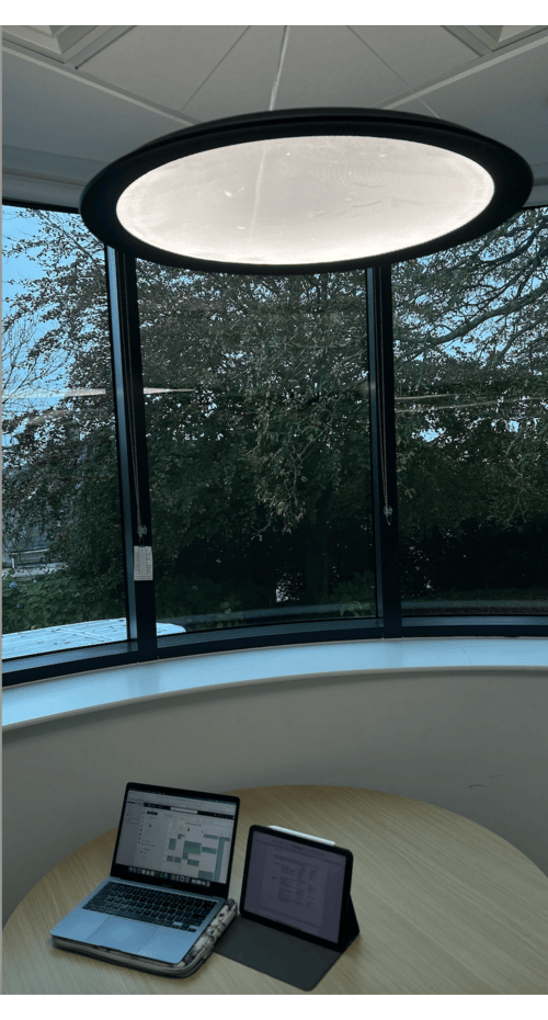 A laptop and tablet on a wooden table surrounded by windows looking out over trees