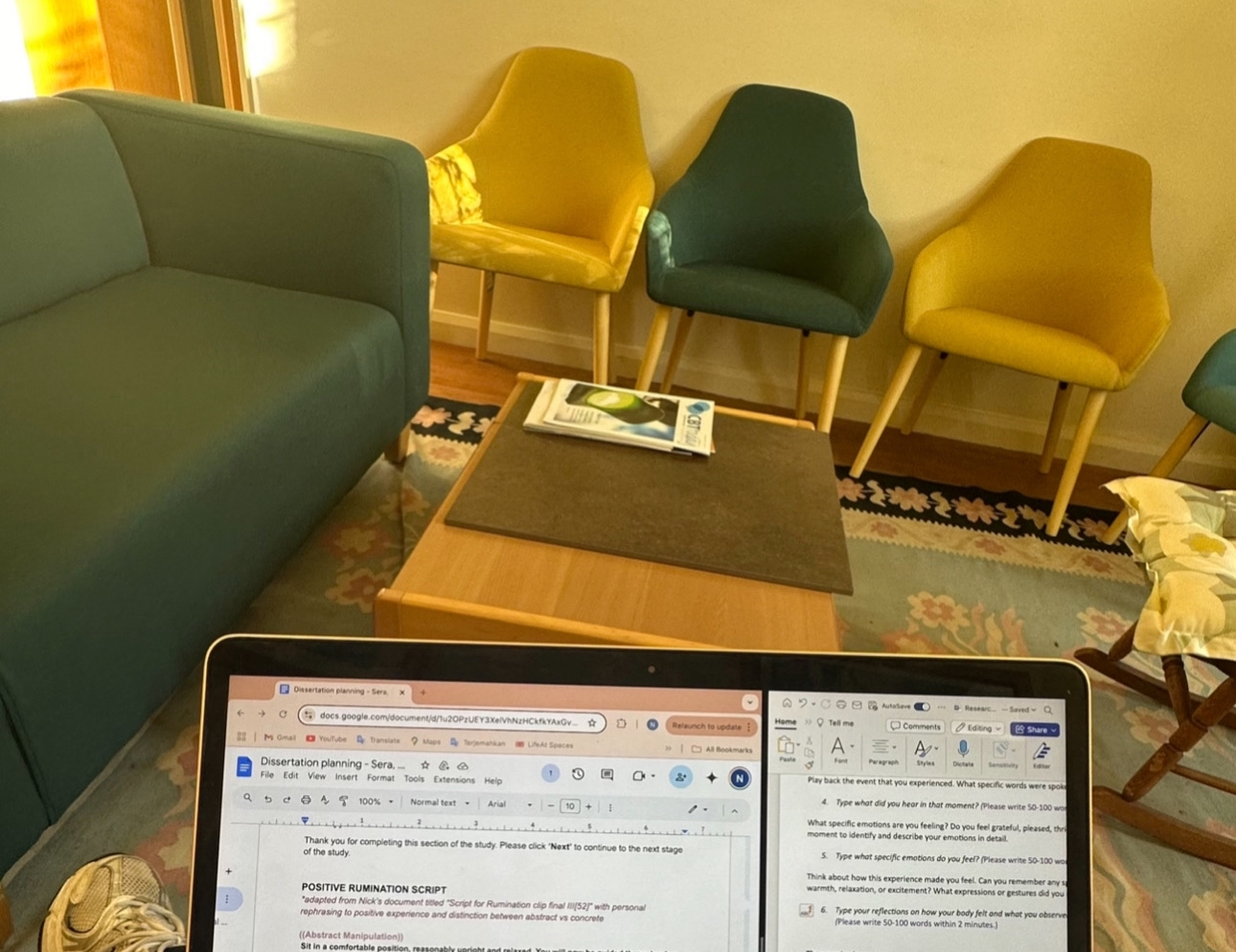 A cozy study space with colorful chairs, a teal sofa, and a laptop displaying dissertation planning documents on a coffee table.