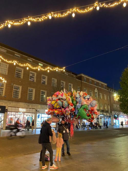 Man holding a big bunch of multicoloured balloons on an empty city street under Christmas lights