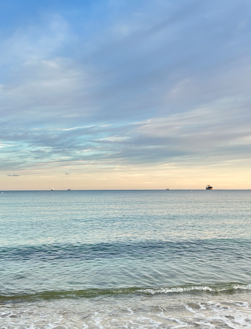 Image of a beach and the sea near to Penryn Campus in Cornwall, with gentle waves and boats on the horizon