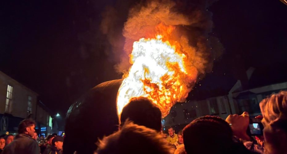 Flaming barrel being carried through a busy crowd in a town square a night