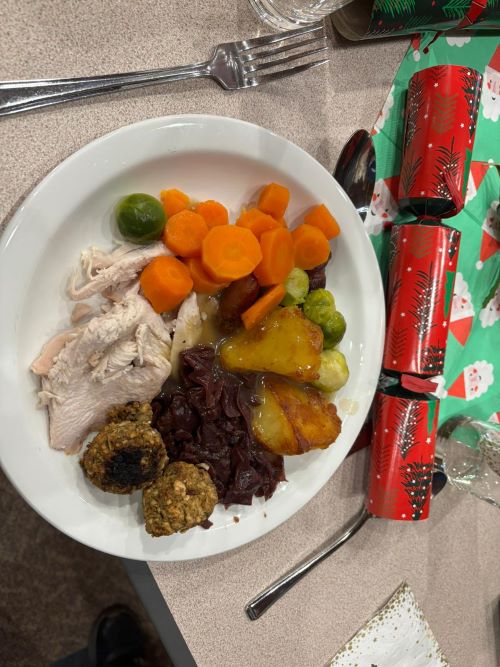 White plate of Christmas dinner, on a table laid with silver cutlery, a red Christmas cracker and a Santa-print napkin 