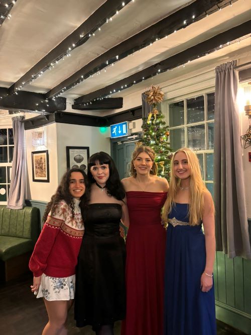 Four female students dressed for a Christmas party posing for a photo in front of a Christmas tree in a traditional English pub