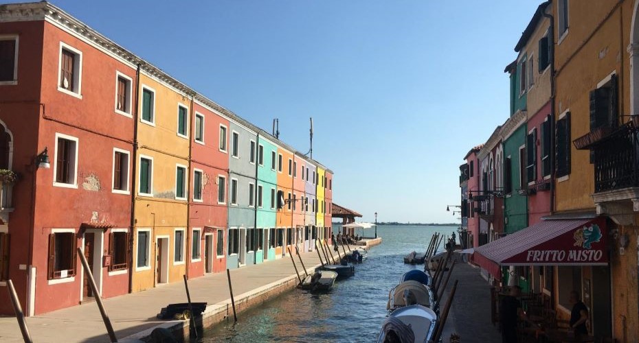 Multicoloured buildings bordering a quiet canal beneath a bright blue sky