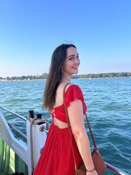 Girl in a red dress standing on a boat turning round to smile at the camera