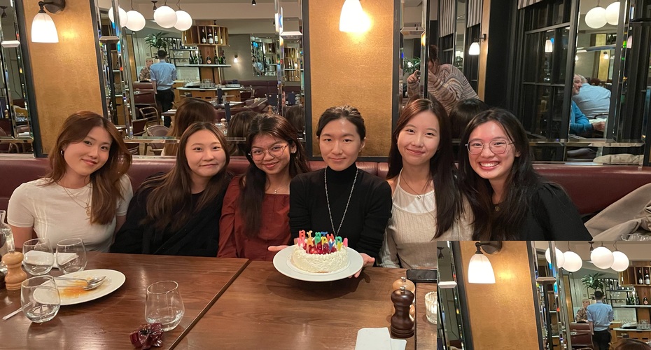 A group of female students sat at a restaurant table behind a decorated birthday cake