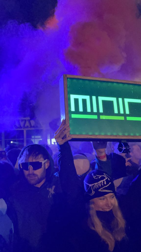 Boy and girl holding up flares and signs at a festival. Nighttime setting with pink and purple colours