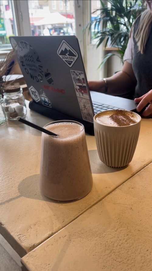 An iced coffee and a cappuccino on a table with a laptop